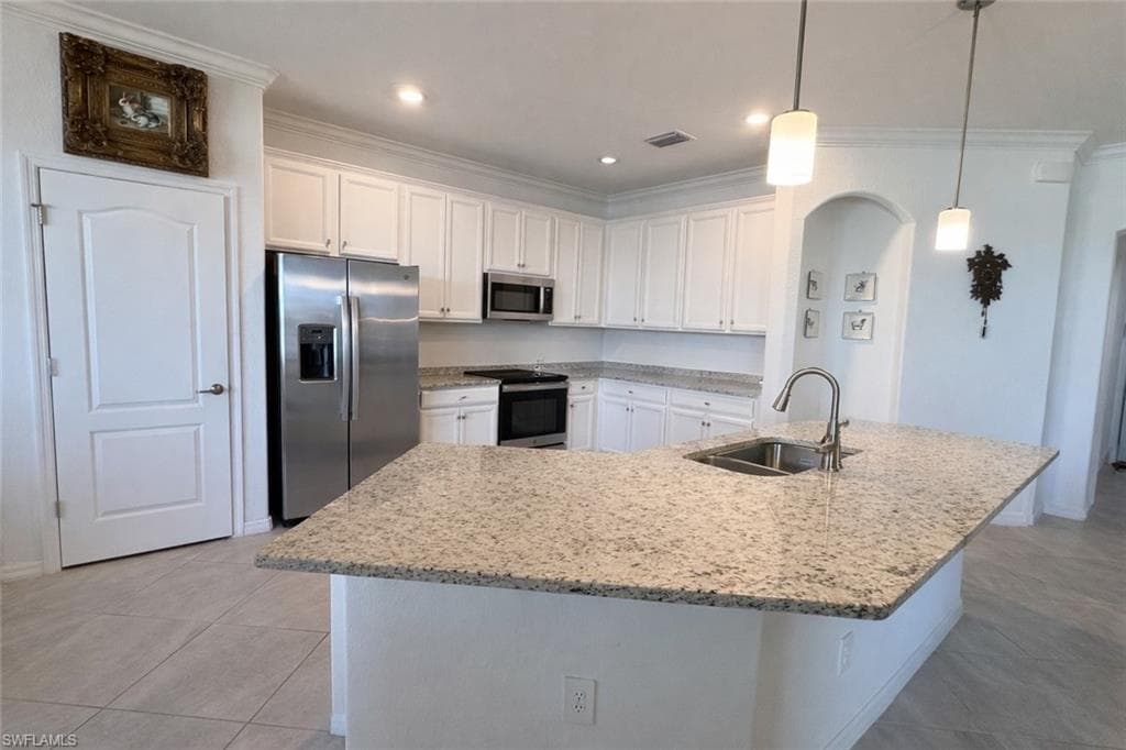 Kitchen with stainless steel appliances, ornamental molding, white cabinetry, light stone counters, and an island with sink