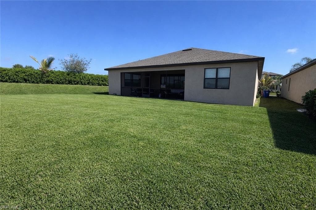 Rear view of house with a lawn, stucco siding, a sunroom, and roof with shingles