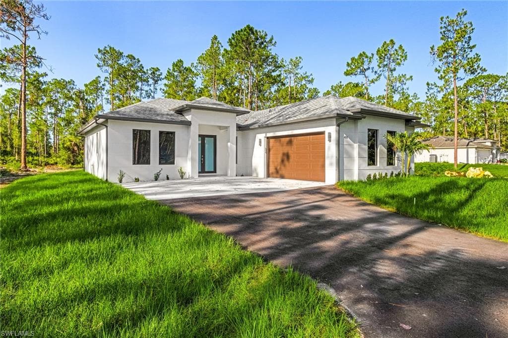 Prairie-style house featuring stucco siding, a garage, driveway, and a front lawn