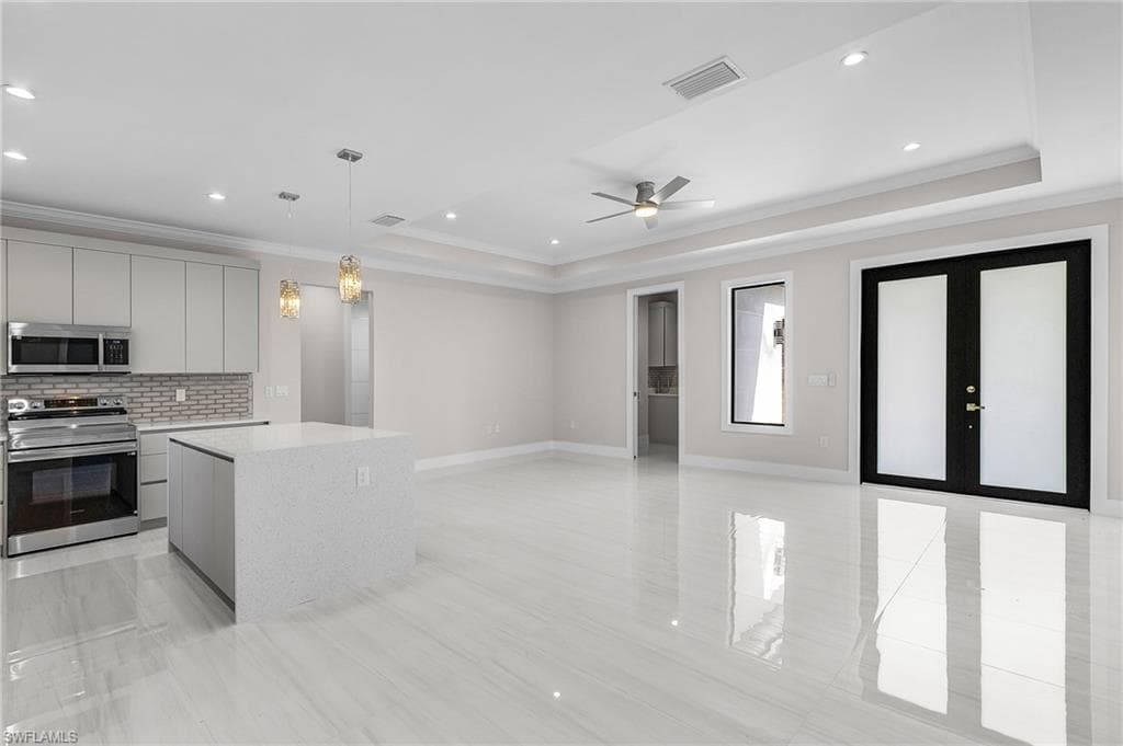 Kitchen featuring stainless steel appliances, decorative light fixtures, open floor plan, crown molding, and light stone countertops