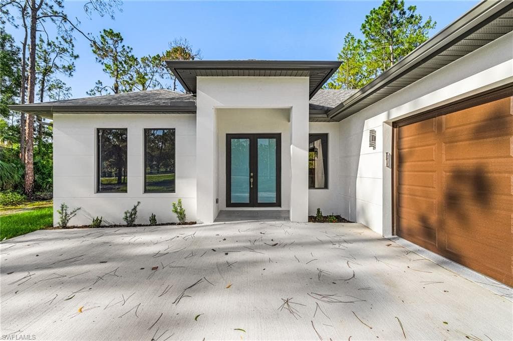 Entrance to property featuring a shingled roof, stucco siding, concrete driveway, french doors, and an attached garage
