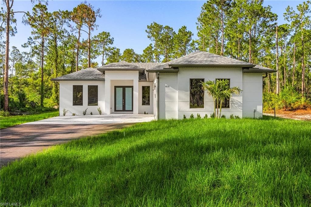View of front of home featuring french doors, stucco siding, driveway, and a front lawn