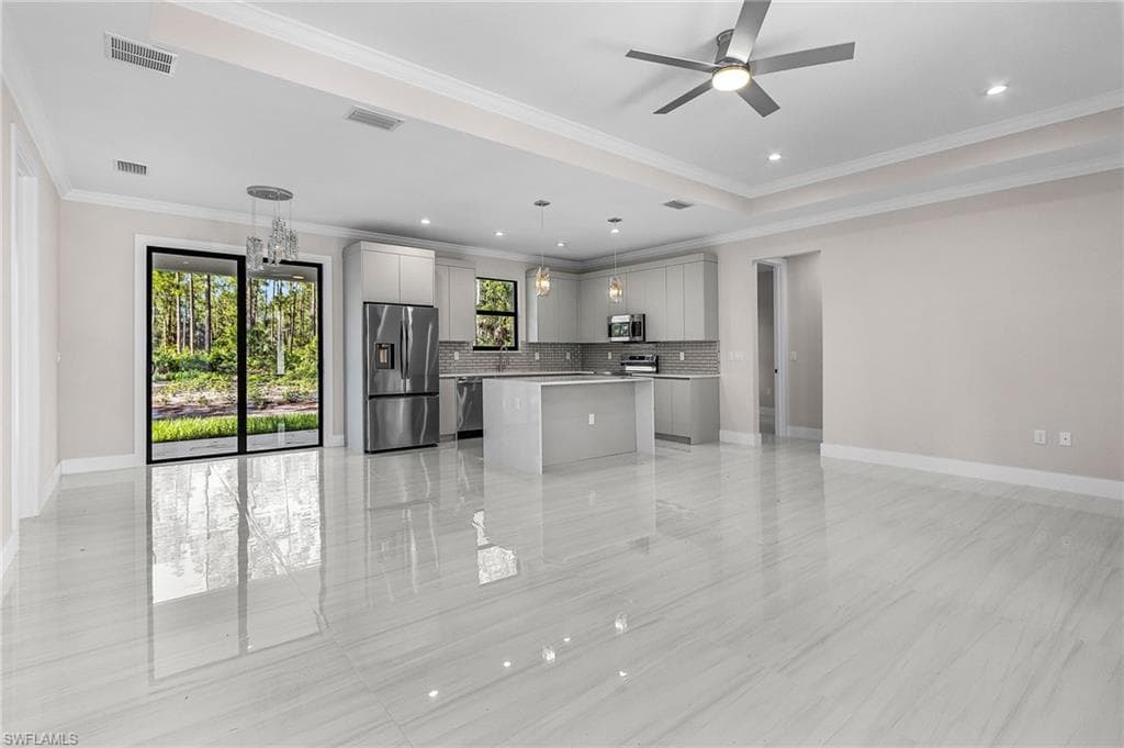 Kitchen featuring open floor plan, a kitchen island, appliances with stainless steel finishes, gray cabinetry, and ornamental molding