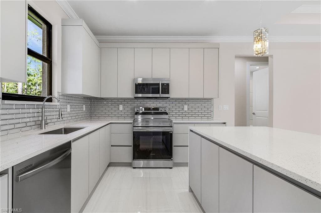 Kitchen with appliances with stainless steel finishes, modern cabinets, light stone counters, and ornamental molding
