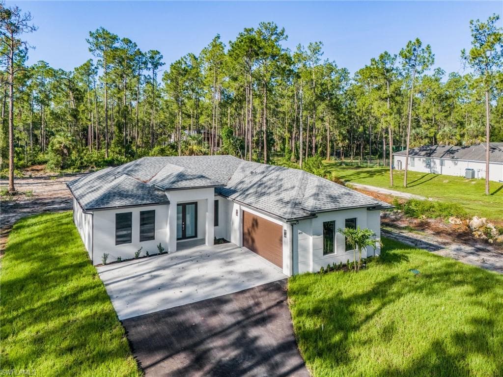 View of front of property featuring a shingled roof, a front lawn, driveway, and an attached garage