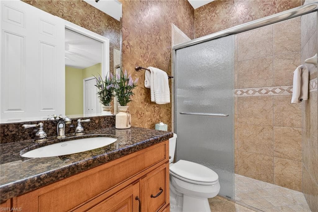 Full bathroom featuring vanity, a tile shower, and wallpapered walls