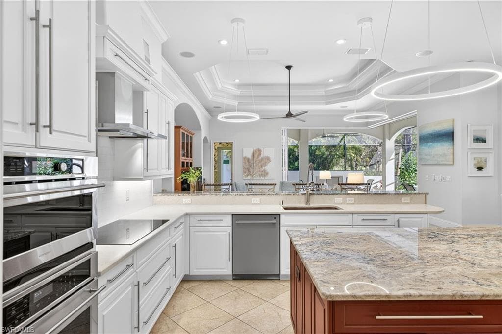 Kitchen featuring light stone countertops, stainless steel appliances, ceiling fan, decorative light fixtures, and two tone cabinetry