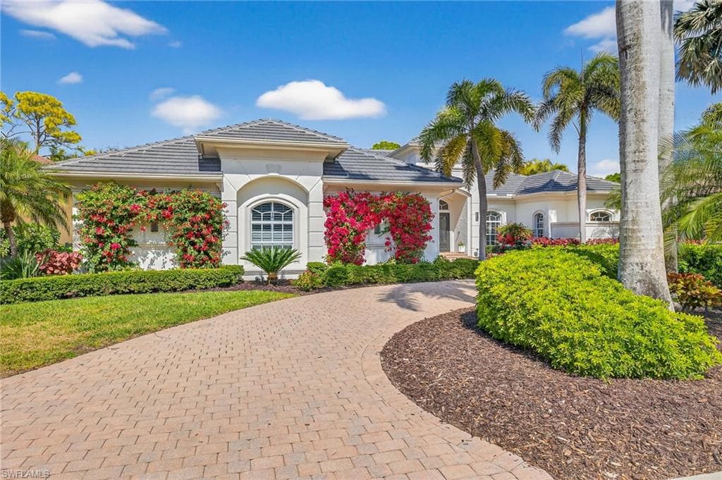 View of front facade featuring a tile roof, stucco siding, and curved driveway