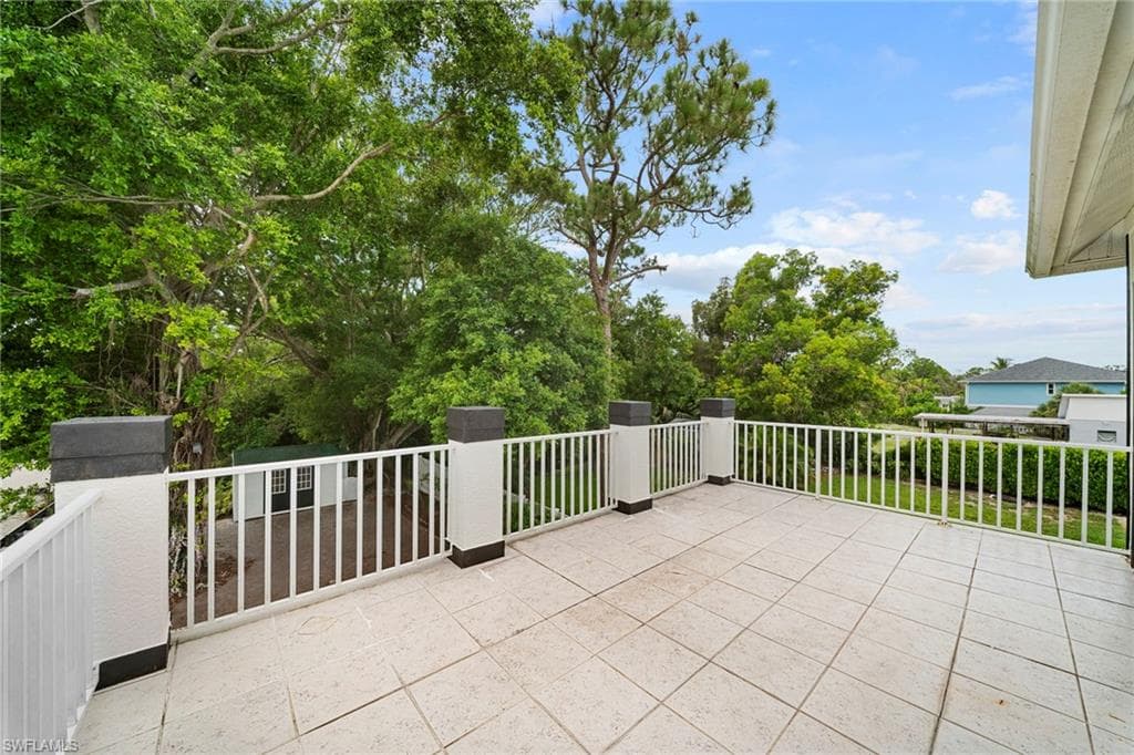 Expansive outdoor terrace featuring light-toned square tile flooring, white vertical balusters, and substantial white pillars with dark caps