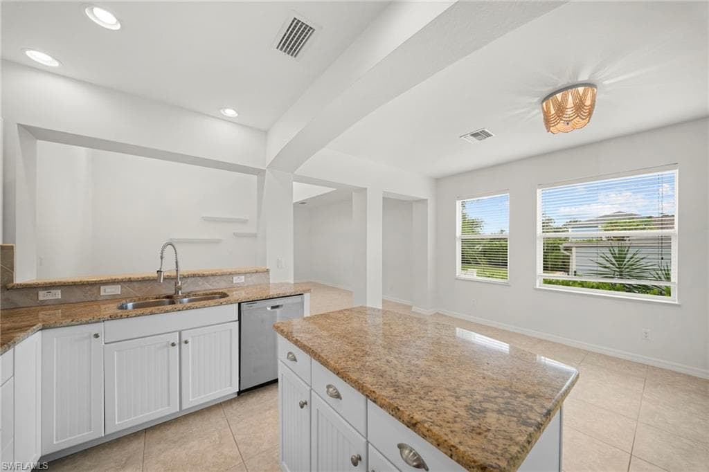 Kitchen featuring a central island, granite countertops, white cabinetry with beadboard detailing, and a stainless steel dishwasher