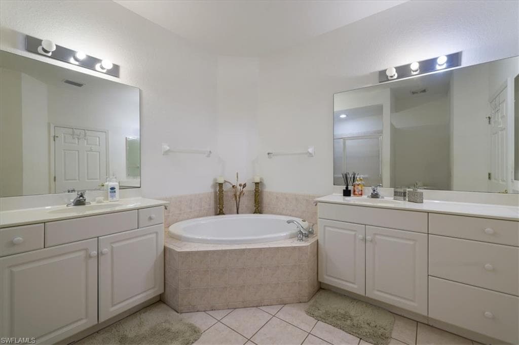 Full bath featuring two vanities, a garden tub, a stall shower, and light tile patterned flooring