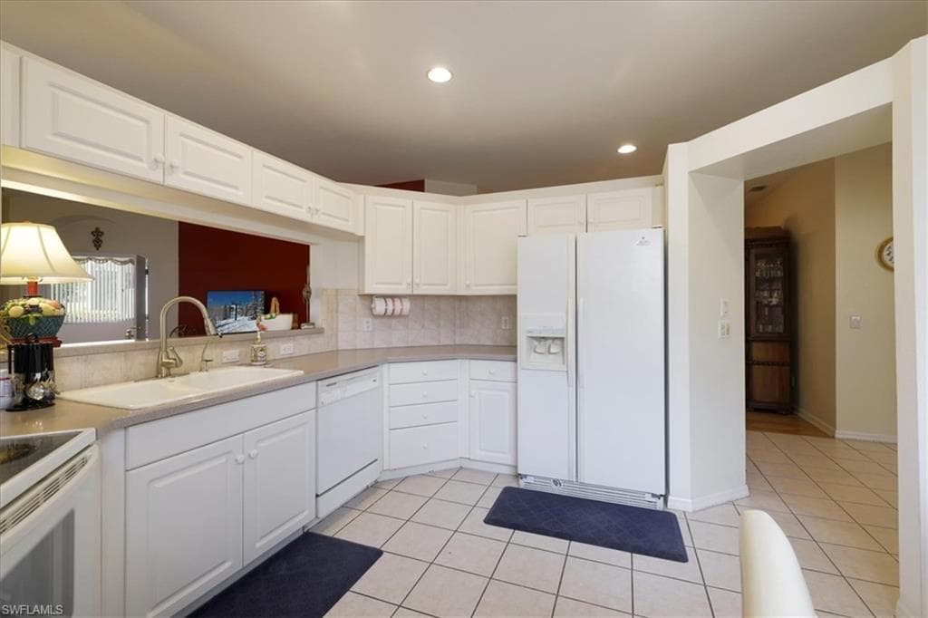 Kitchen with white appliances, white cabinets, light countertops, light tile patterned flooring, and backsplash