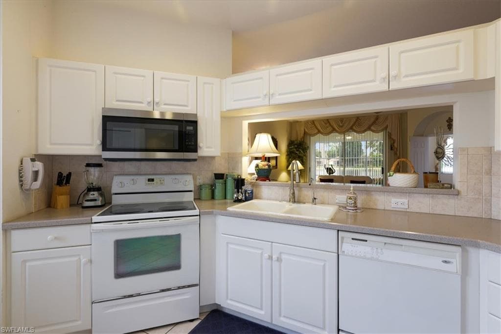 Kitchen with white appliances, white cabinets, and tasteful backsplash