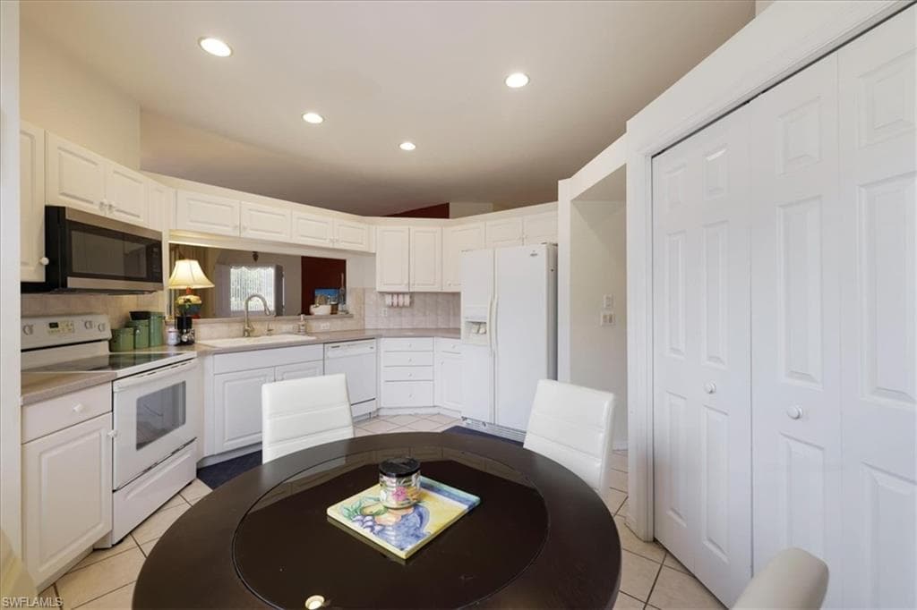 Kitchen with white appliances, tasteful backsplash, light countertops, white cabinets, and recessed lighting