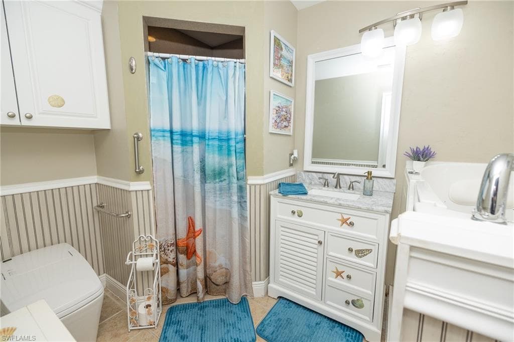Bathroom with a shower with curtain, vanity, and wainscoting