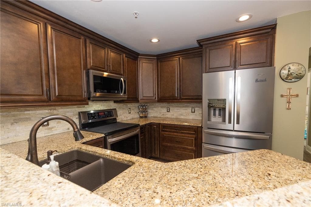 Kitchen with stainless steel appliances, dark wood finish cabinetry, light stone counters, recessed lighting, and tasteful backsplash
