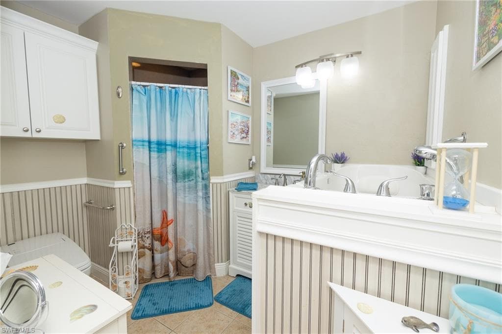 Bathroom with double vanity, curtained shower, wainscoting, and light tile patterned flooring