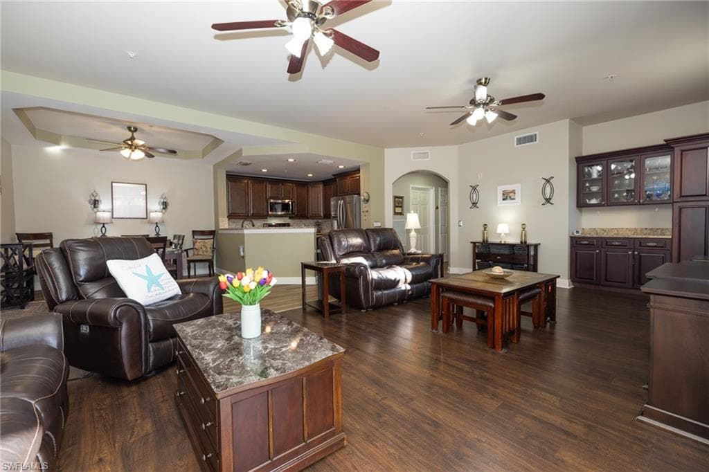 Living room with arched walkways, ceiling fan, a raised ceiling, dark wood-style flooring, and recessed lighting