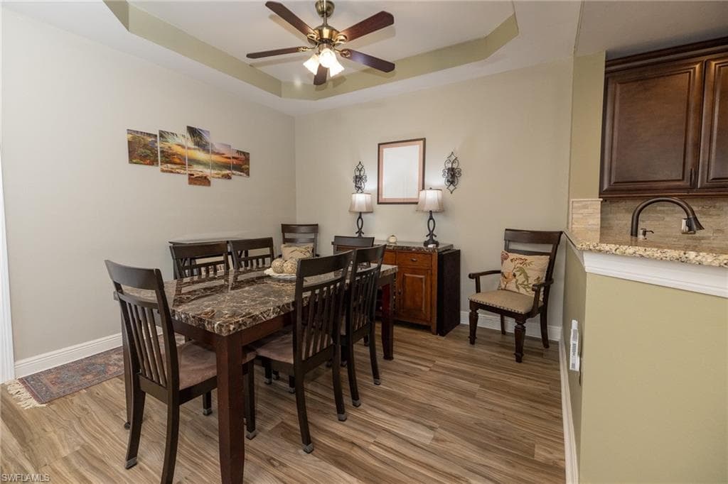 Dining room featuring light wood-style floors, a tray ceiling, and a ceiling fan