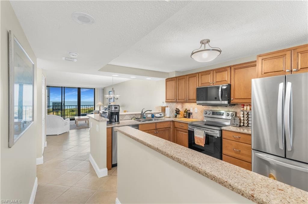 Kitchen with stainless steel appliances, a peninsula, wood finish cabinetry, light tile patterned flooring, and hanging light fixtures