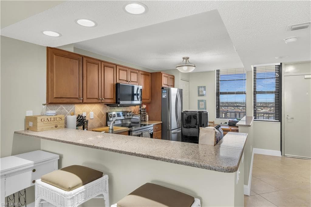 Kitchen featuring a peninsula, a kitchen breakfast bar, tasteful backsplash, stainless steel appliances, and wood finish cabinets