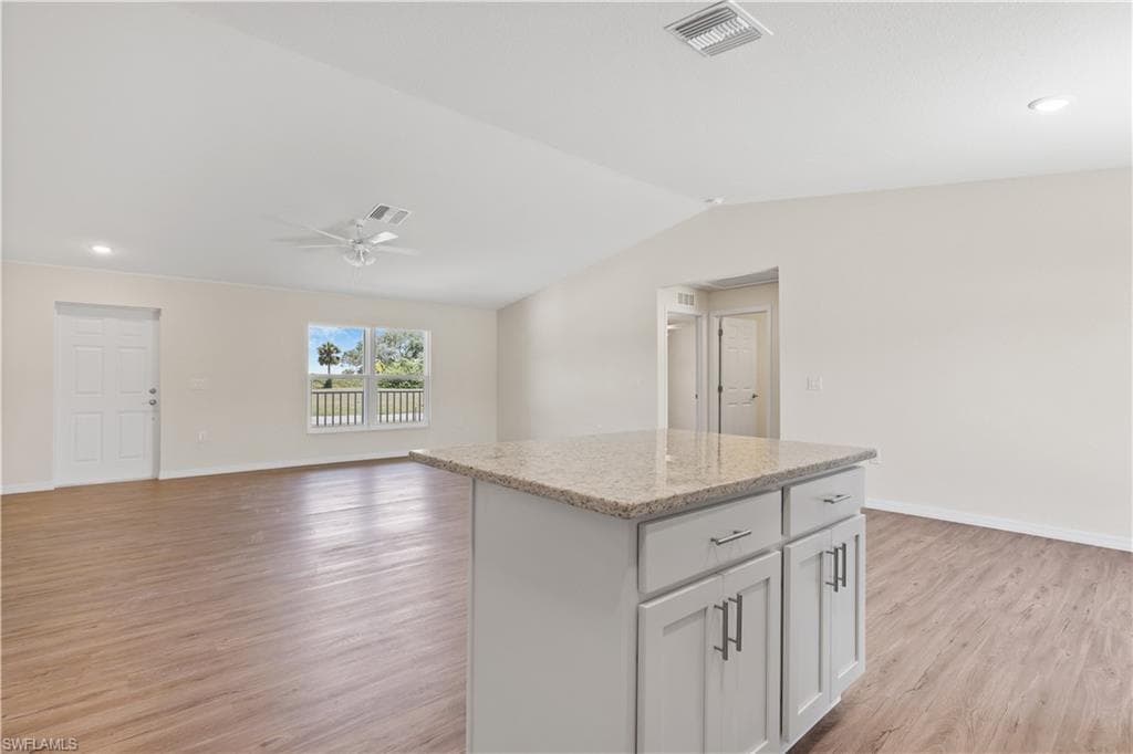 Kitchen featuring a kitchen island, light stone counters, open floor plan, white cabinets, and light wood finished floors