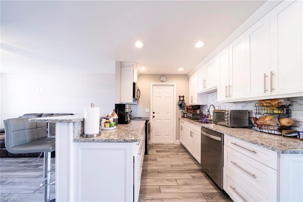 Kitchen featuring light stone countertops, white cabinets, a kitchen breakfast bar, stainless steel appliances, and recessed lighting