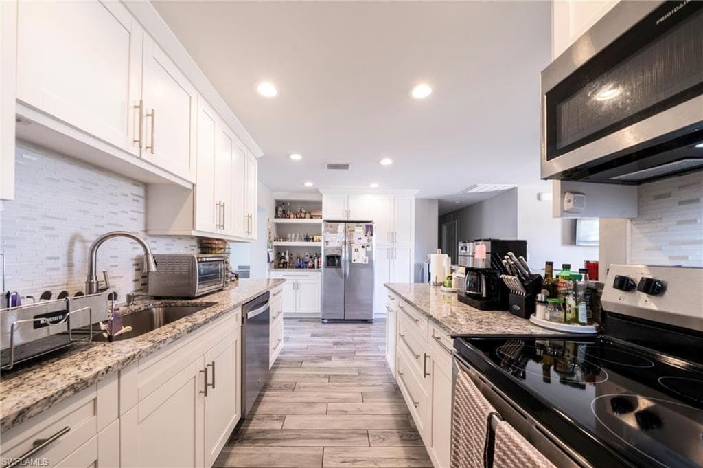 Kitchen with backsplash, stainless steel appliances, white cabinetry, light wood-type flooring, and light stone counters