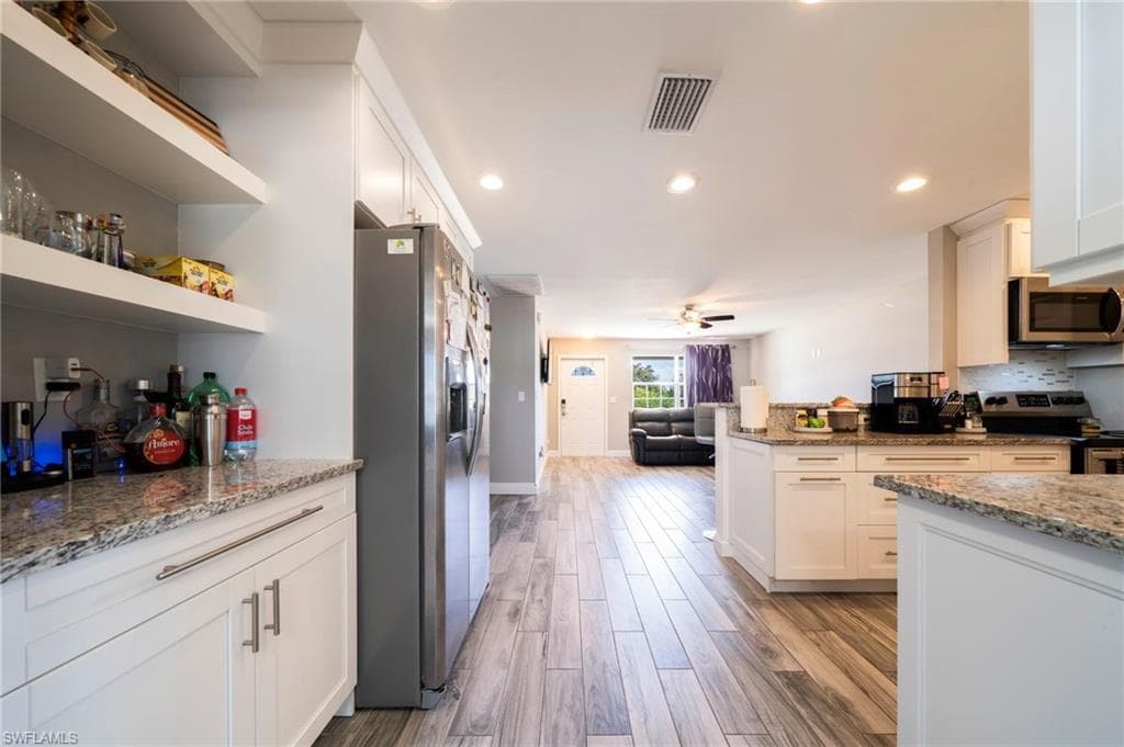 Kitchen with open shelves, light stone counters, open floor plan, white cabinets, and stainless steel appliances