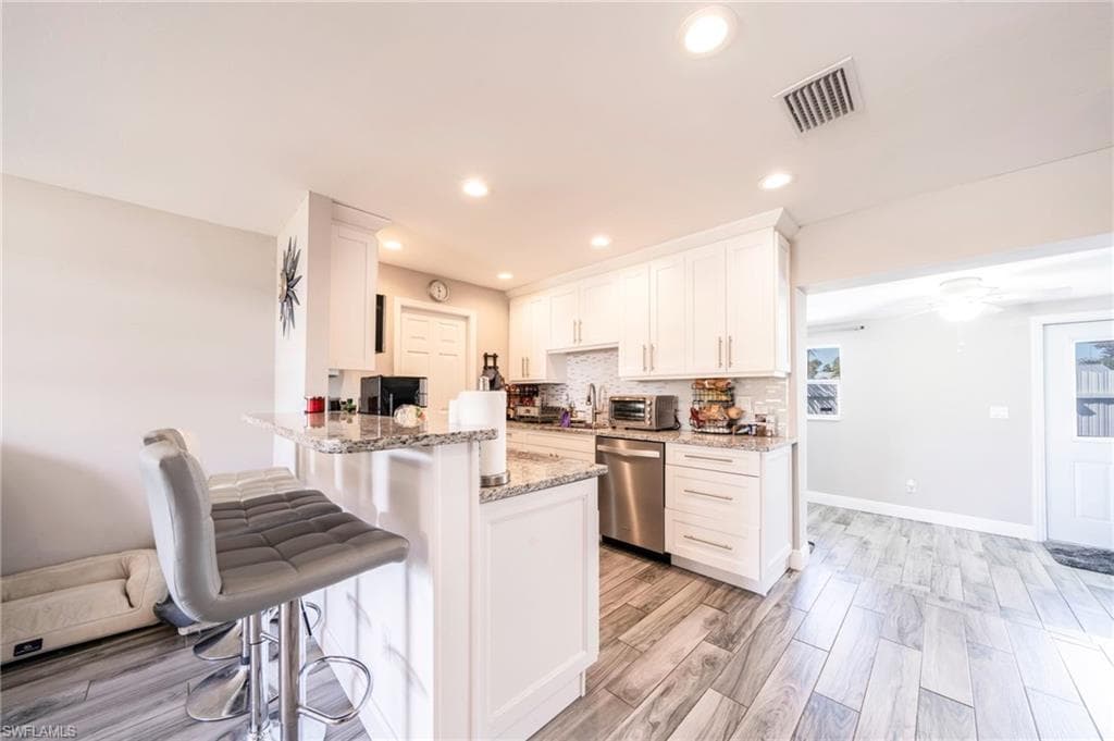 Kitchen featuring white cabinets, light stone counters, a kitchen breakfast bar, tasteful backsplash, and wood finish floors