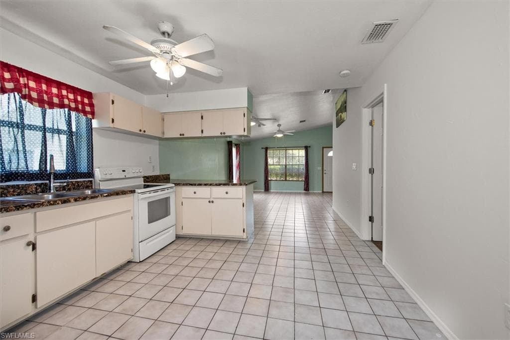 Kitchen with white range with electric cooktop, a peninsula, ceiling fan, open floor plan, and light tile patterned floors