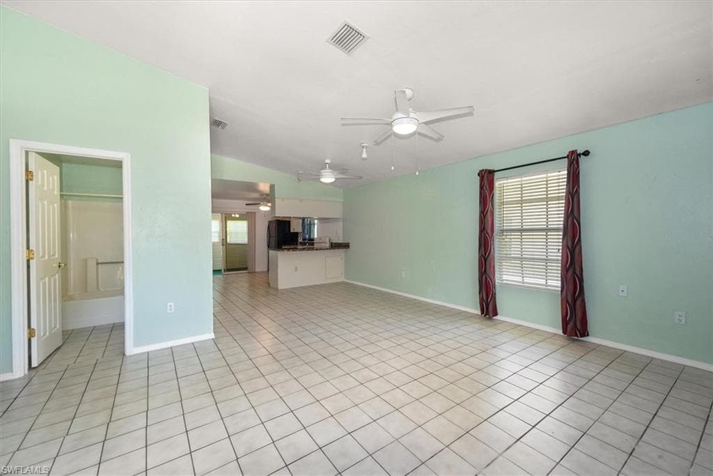 Unfurnished living room with a ceiling fan, vaulted ceiling, and light tile patterned floors