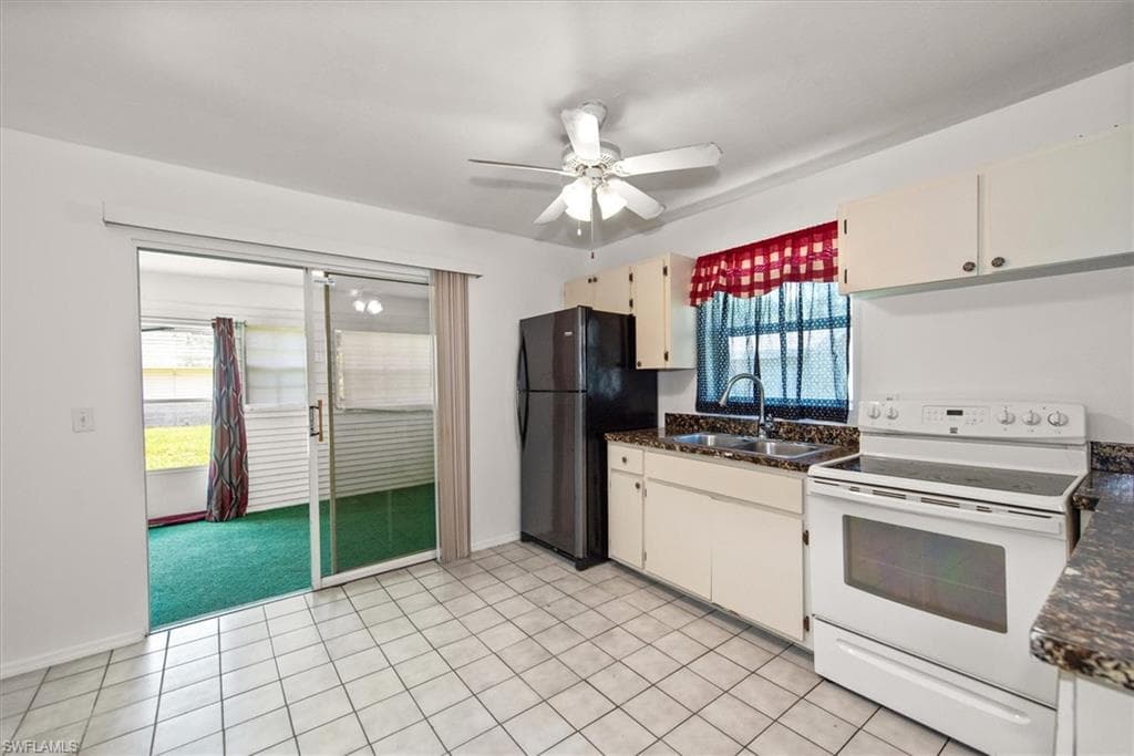 Kitchen featuring white electric stove, ceiling fan, freestanding refrigerator, light tile patterned floors, and dark stone counters