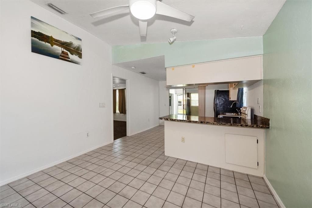 Kitchen with lofted ceiling, light tile patterned floors, dark stone counters, a peninsula, and a ceiling fan