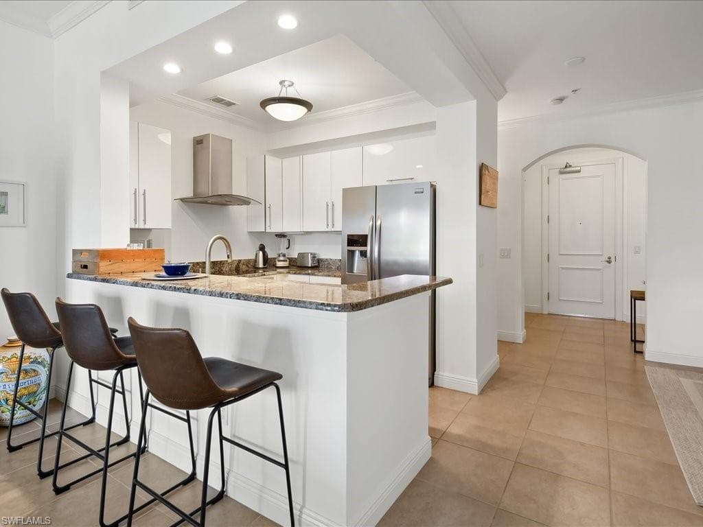 Kitchen featuring ornamental molding, arched walkways, white cabinets, light tile patterned flooring, and a peninsula