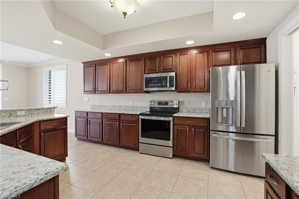 Kitchen featuring stainless steel appliances, granite countertpos, recessed lighting, light tile floors, and a raised ceiling