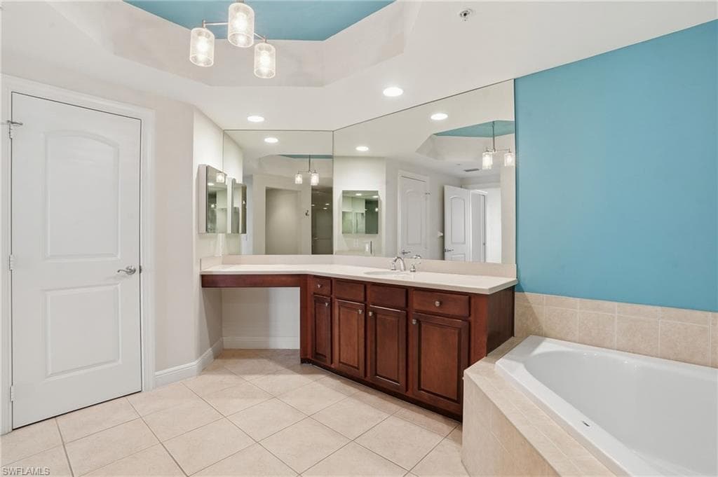 PrimaryBathroom with a tray ceiling, recessed lighting, vanity, light tile patterned flooring, and a bath