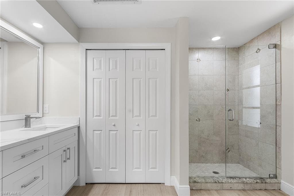 Bathroom with a closet, a stall shower, vanity, recessed lighting, and light wood-type flooring