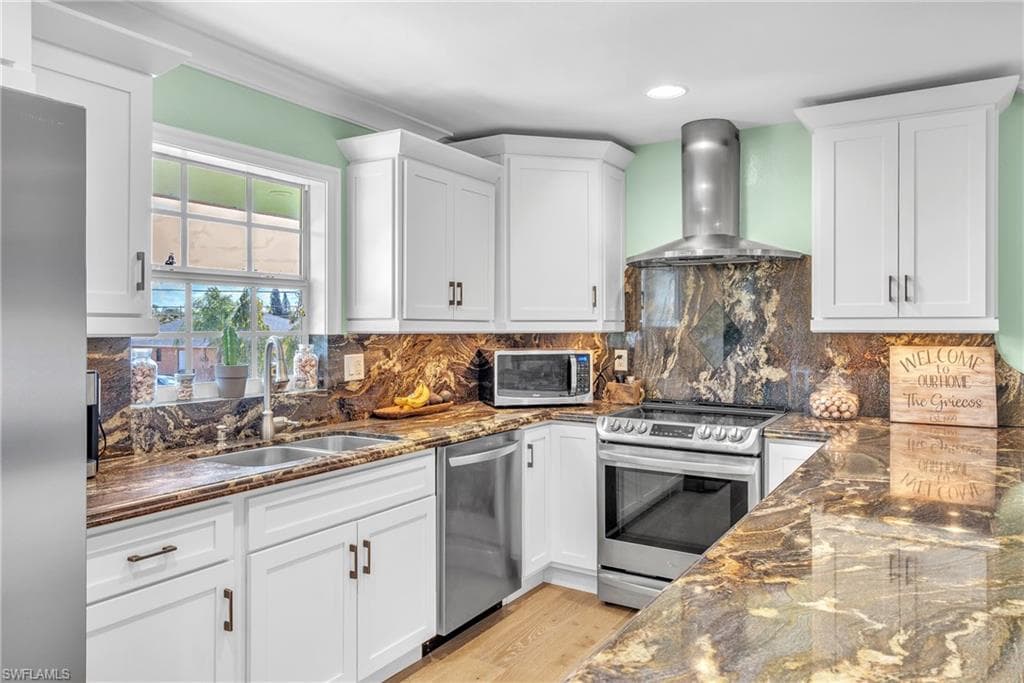 Kitchen with dark stone counters, stainless steel appliances, white cabinets, decorative backsplash, and recessed lighting