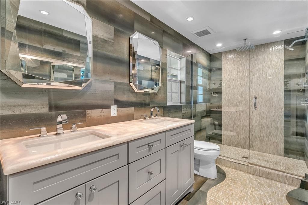 Bathroom featuring double vanity, a shower stall, recessed lighting, and tile walls