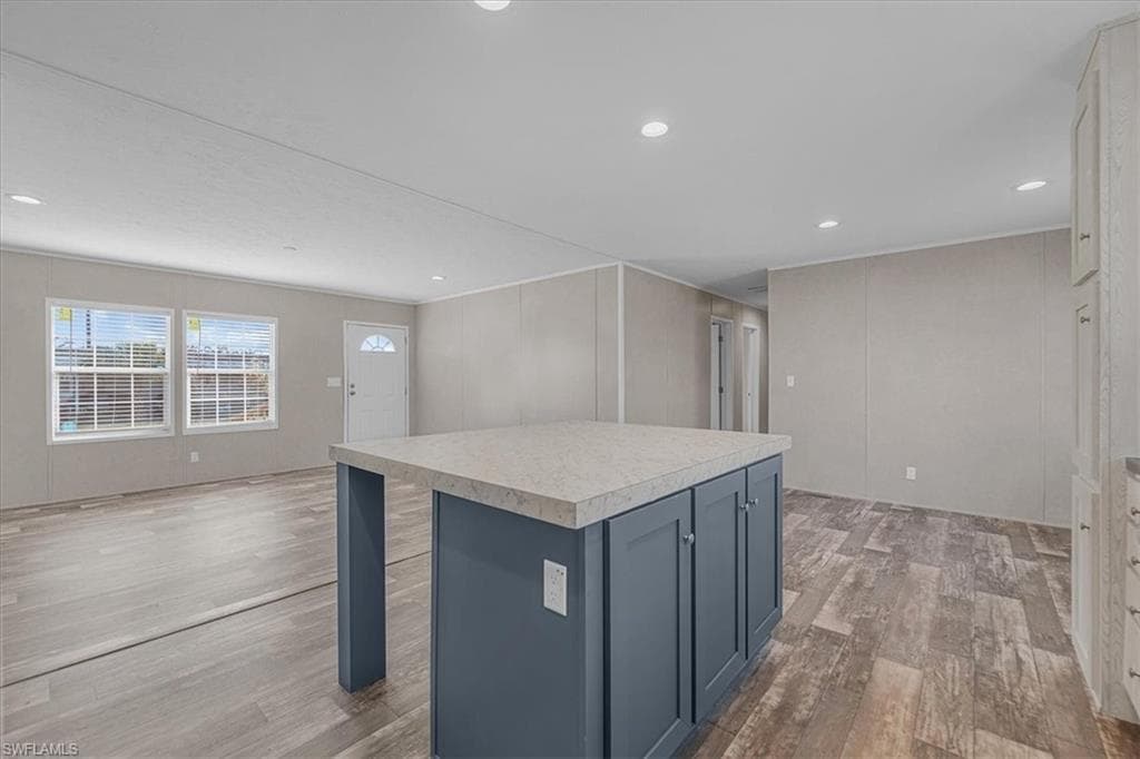 Kitchen with blue cabinets, light countertops, a decorative wall, a kitchen island, and light wood-type flooring