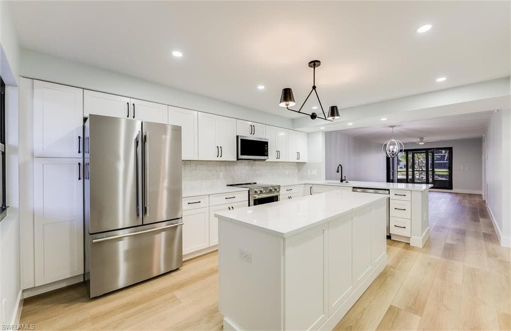 Kitchen with stainless steel appliances, suspended lighting, light wood-type flooring, a peninsula, and white cabinetry
