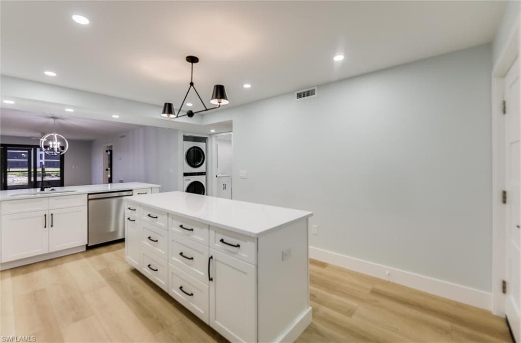Kitchen with stacked washer / dryer, stainless steel dishwasher, white cabinetry, light wood-type flooring, and a chandelier
