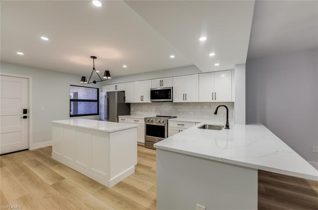Kitchen featuring white cabinetry, stainless steel appliances, a kitchen island, hanging light fixtures, and light stone counters