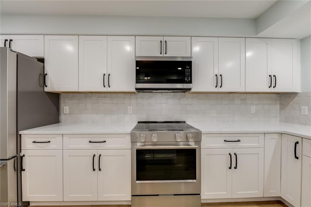 Kitchen with stainless steel appliances, decorative backsplash, light stone counters, and white cabinetry