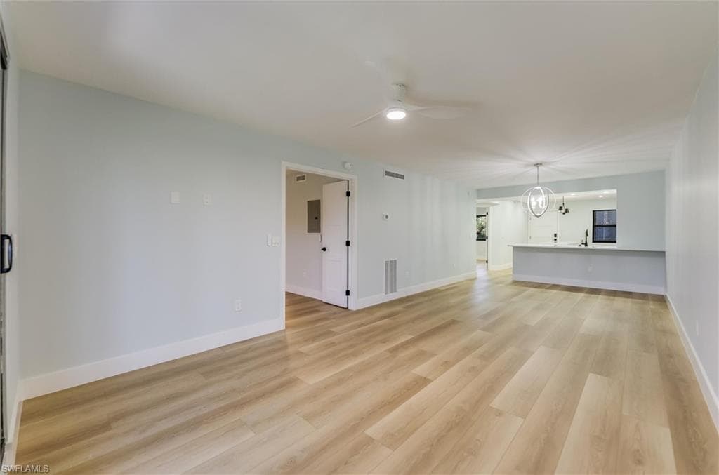 Unfurnished living room featuring ceiling fan, light wood-type flooring, and a chandelier