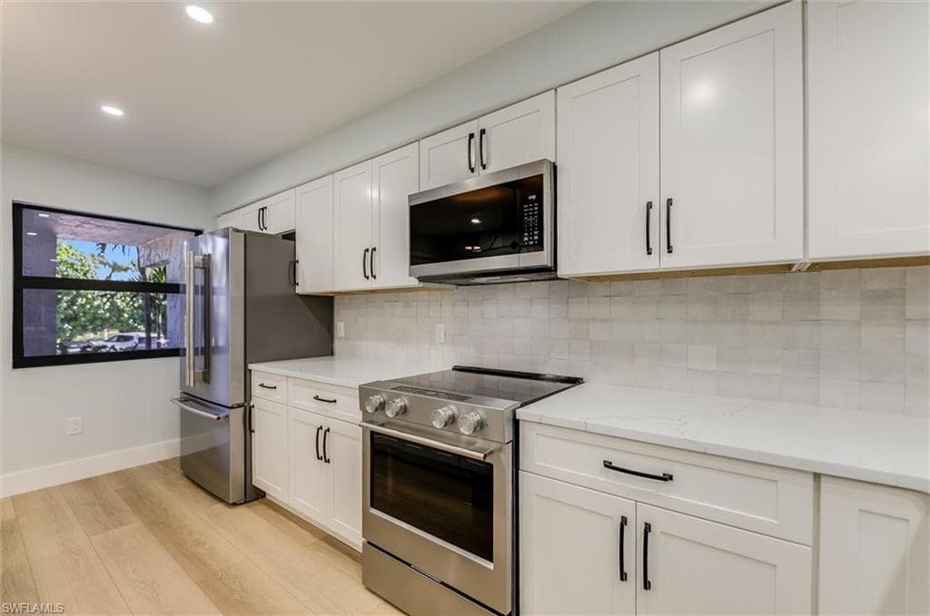 Kitchen with stainless steel appliances, white cabinets, light wood-type flooring, light stone countertops, and recessed lighting