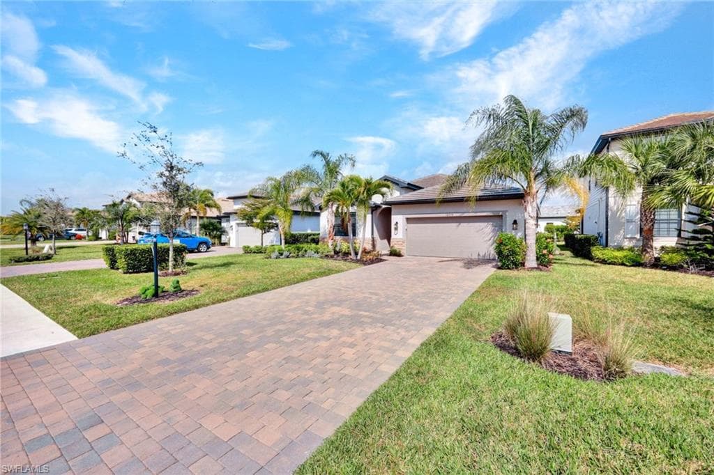 View of front of house featuring decorative driveway, a front lawn, stucco siding, and a garage
