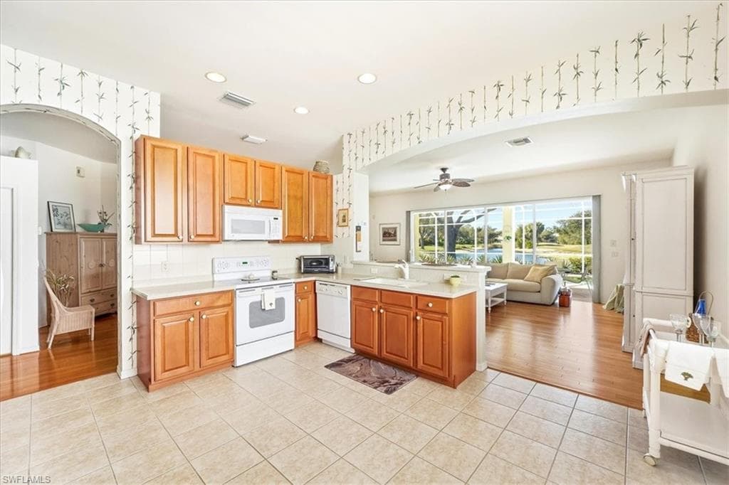 Kitchen featuring arched walkways, wallpapered walls, white appliances, light tile patterned flooring, and open floor plan