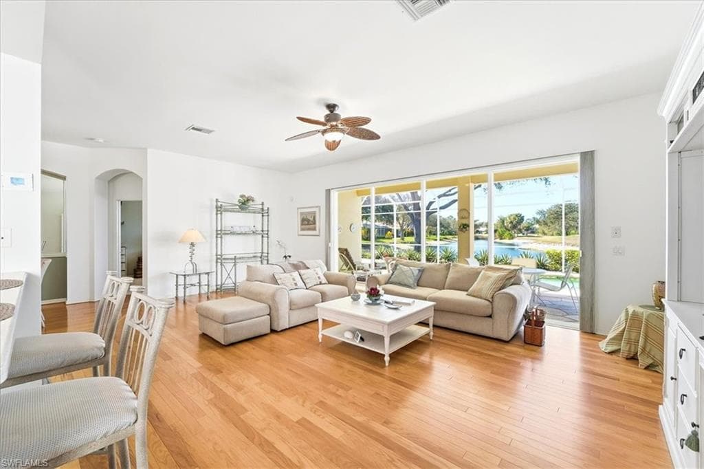 Living area with ceiling fan, light wood-style floors, and arched walkways